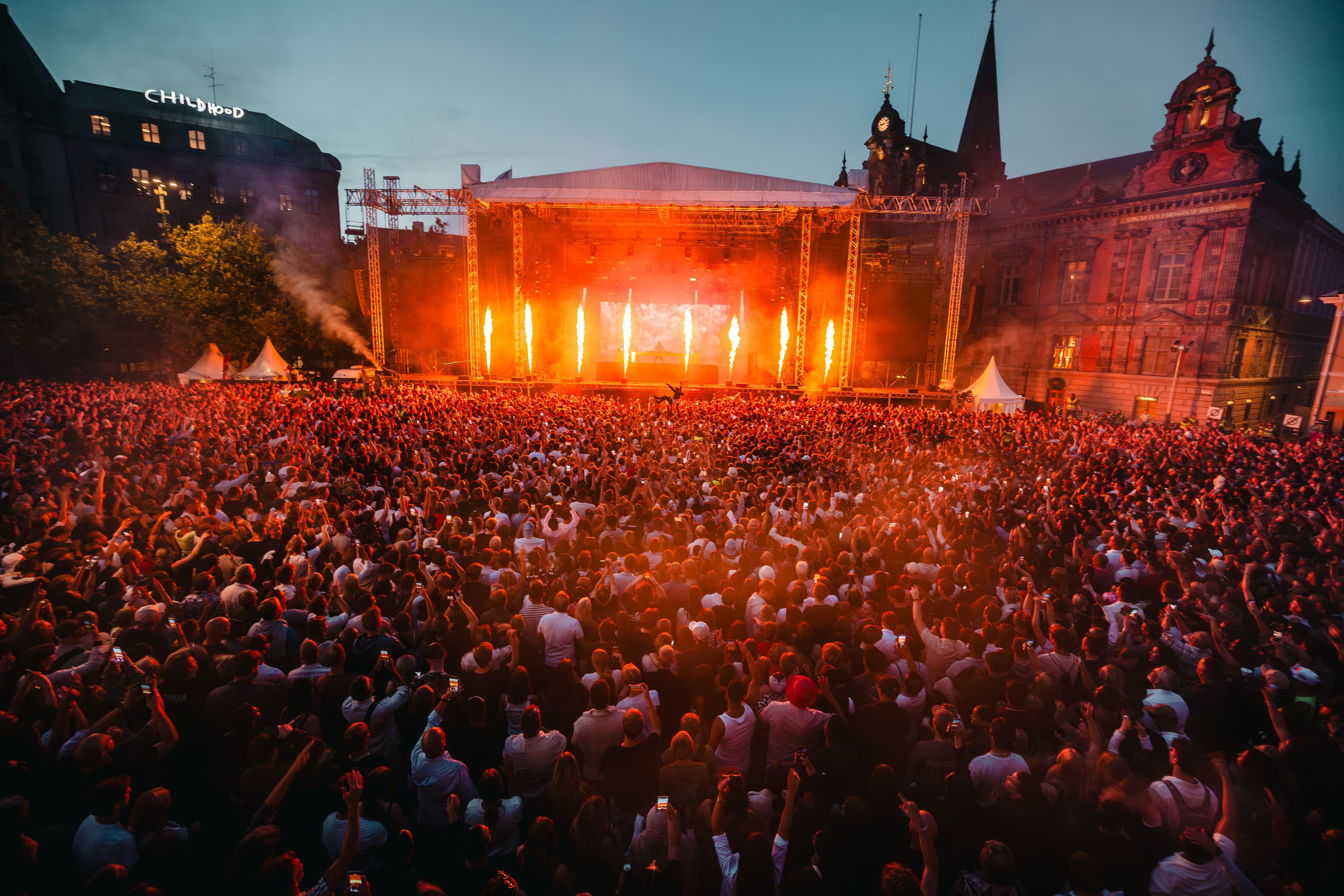 Tät publik framför Stora Scenen upplyst med eldflammor under en konsert på Stortorget i Malmö.