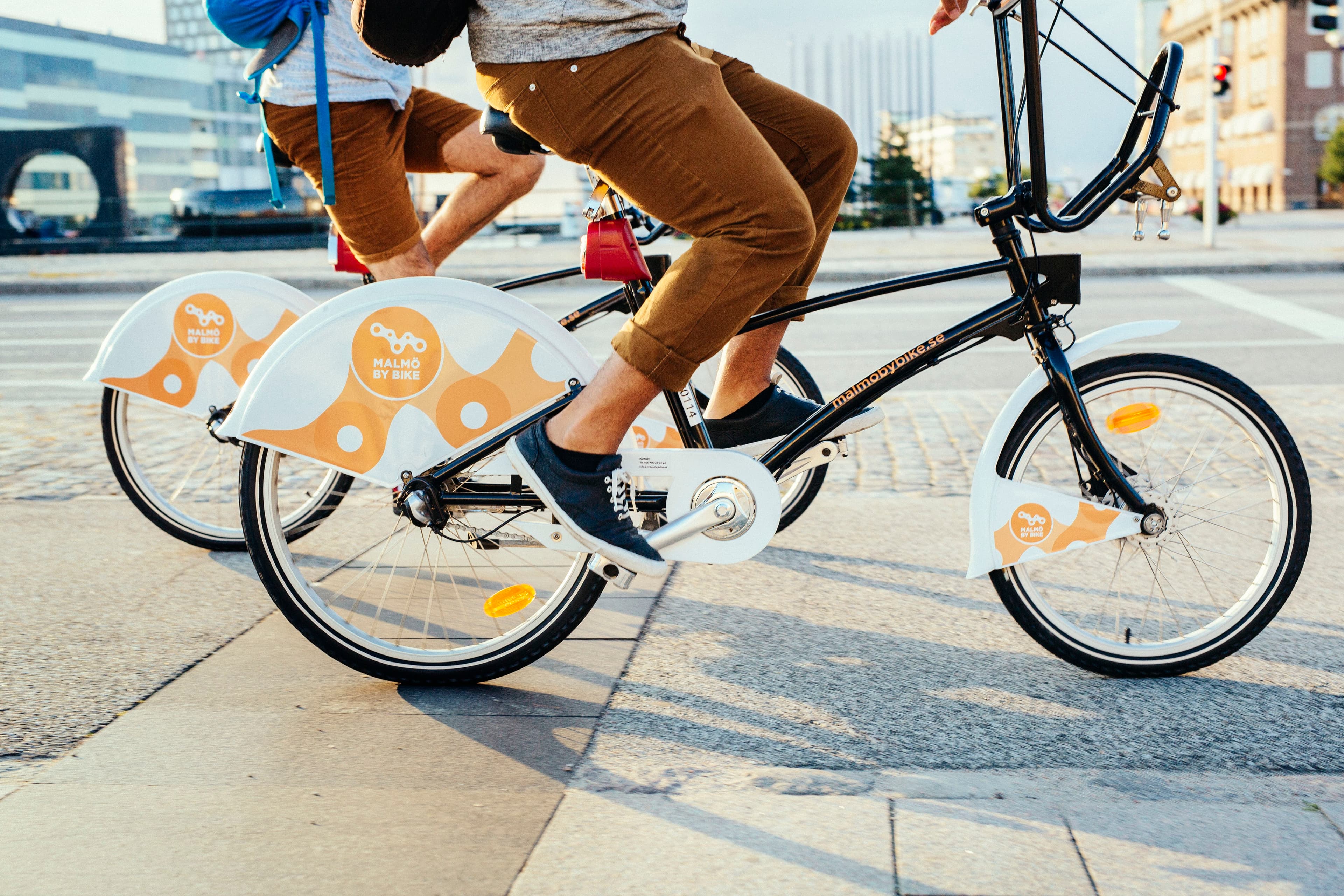 Två personer som cyklar varav den i förgrunden har bruna byxor på sig.