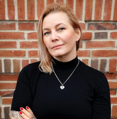 En kvinna i svart tröja står framför en husfasad av tegel.